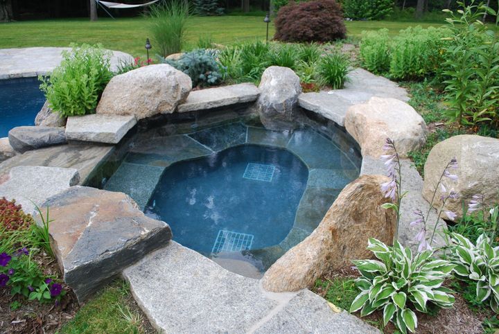 A hot tub surrounded by rocks and plants next to a pool.