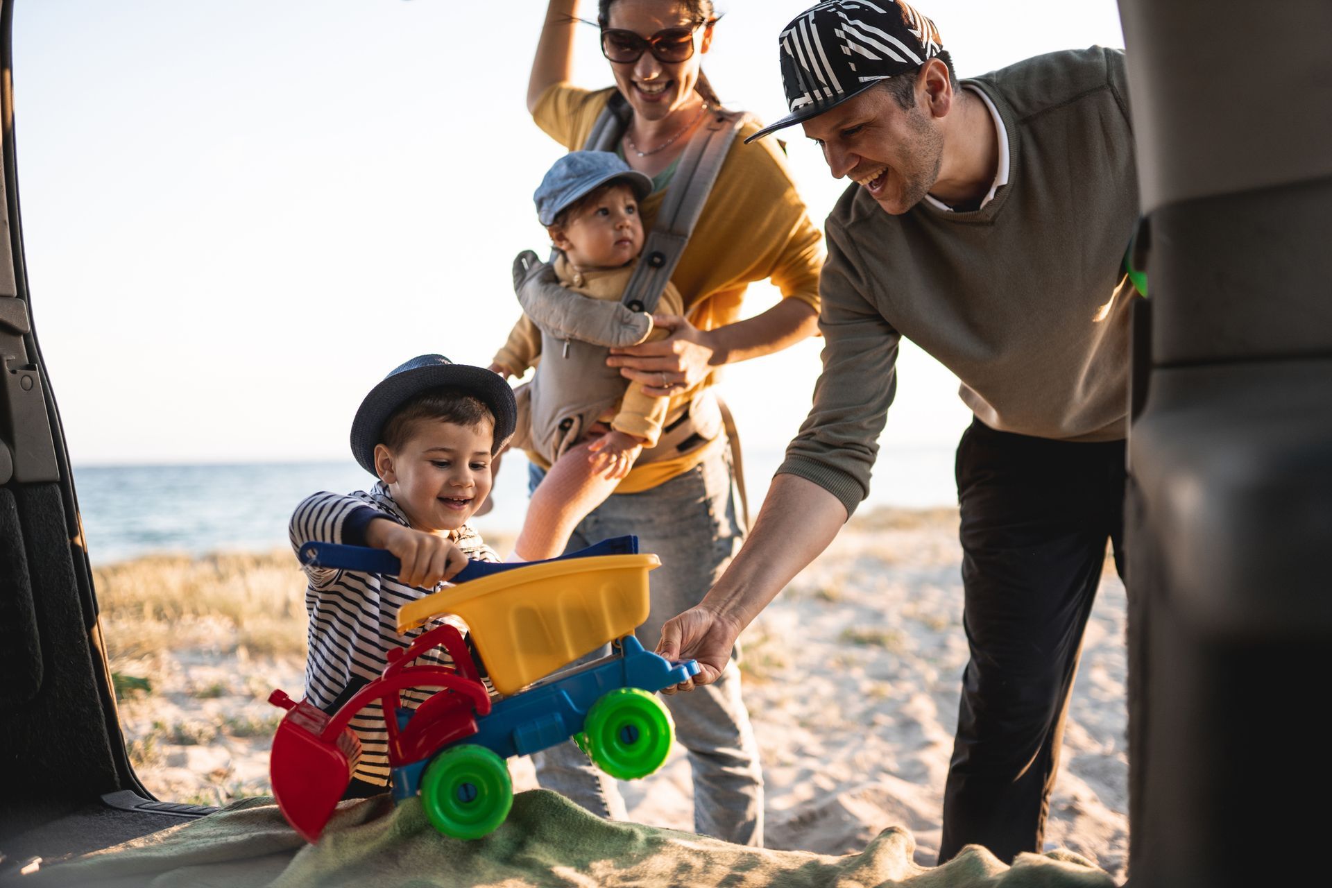 Woman in a blue shirt reads a book while relaxing on a wooden couch in a sunlit, tropical setting.