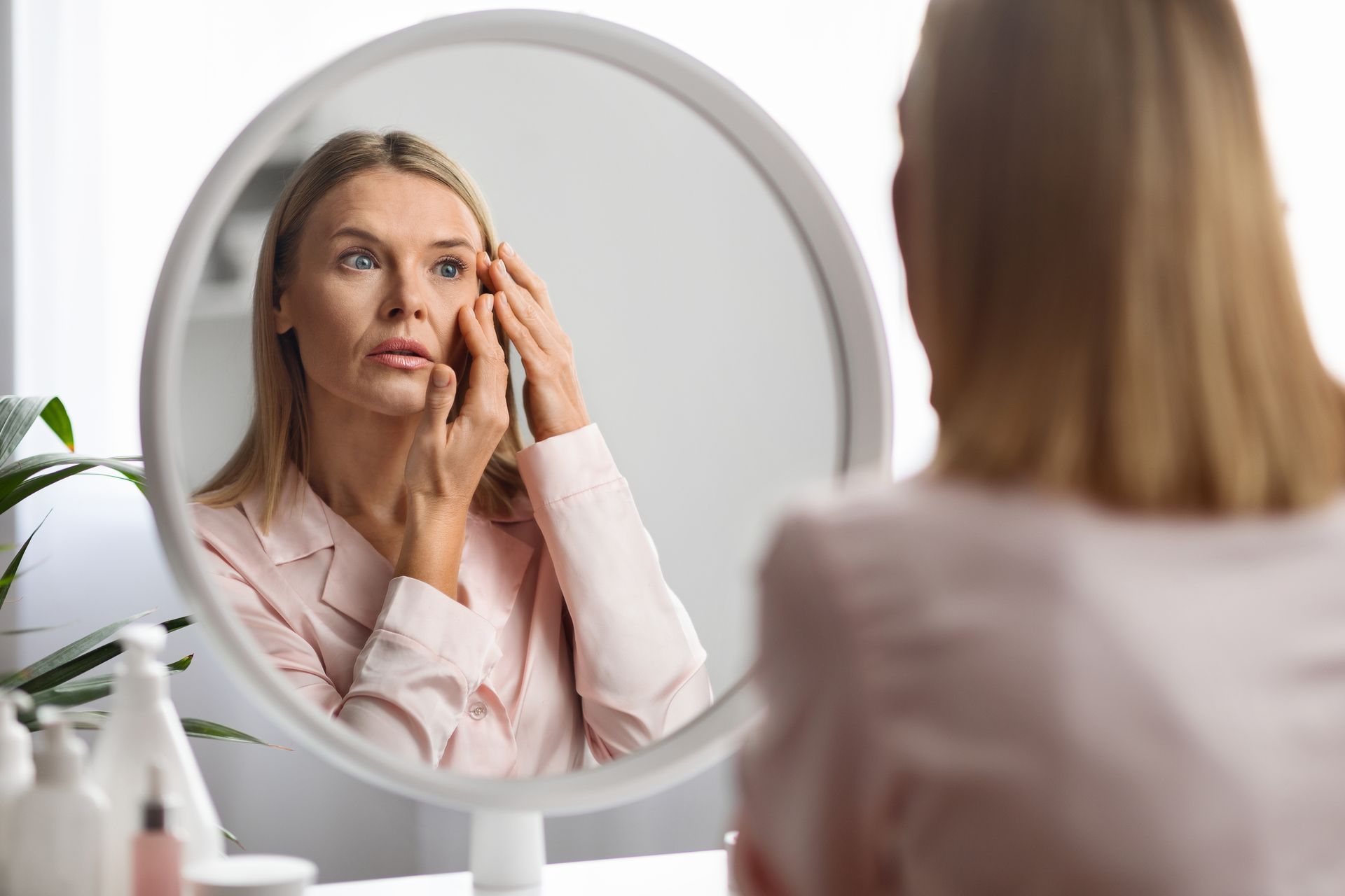 Woman applying facial cream while looking in a mirror in a bright bathroom
