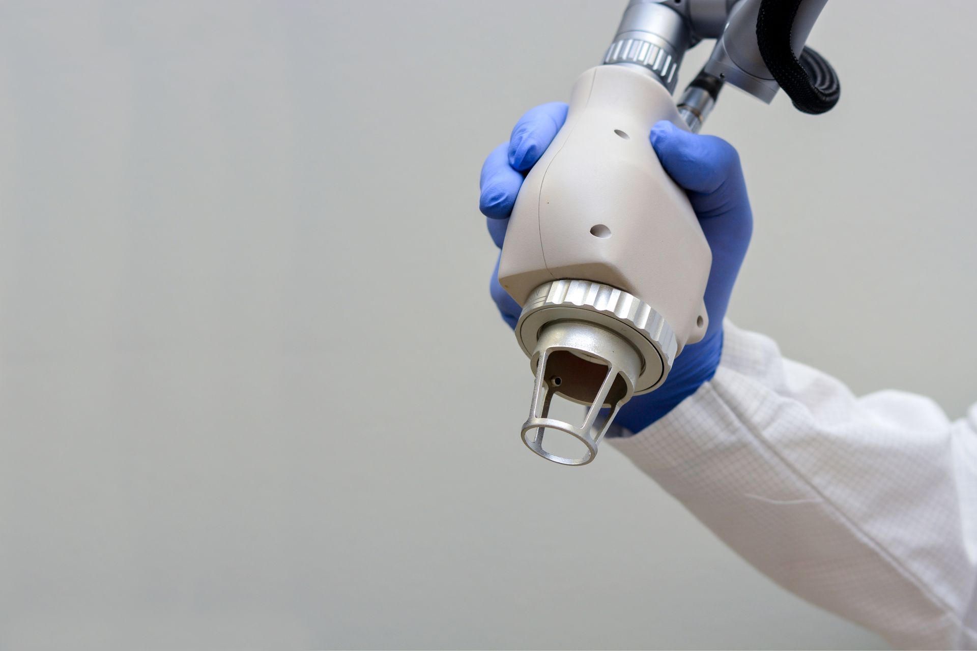 Gloved hand holding a white robotic surgical tool against a plain background