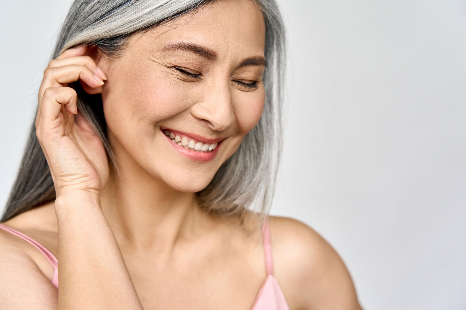 A woman with gray hair is smiling and touching her ear.