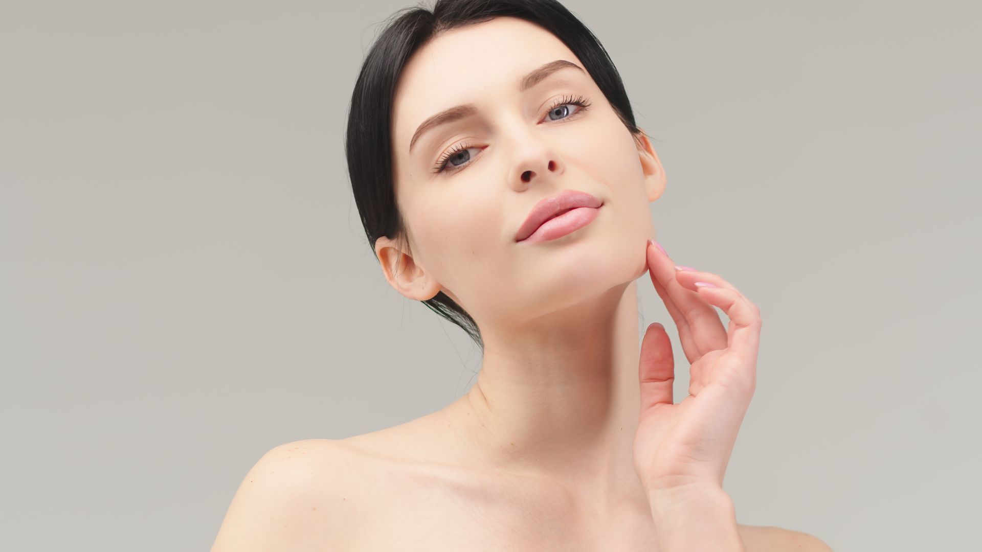 A woman is touching her face with her hand and looking at the camera.