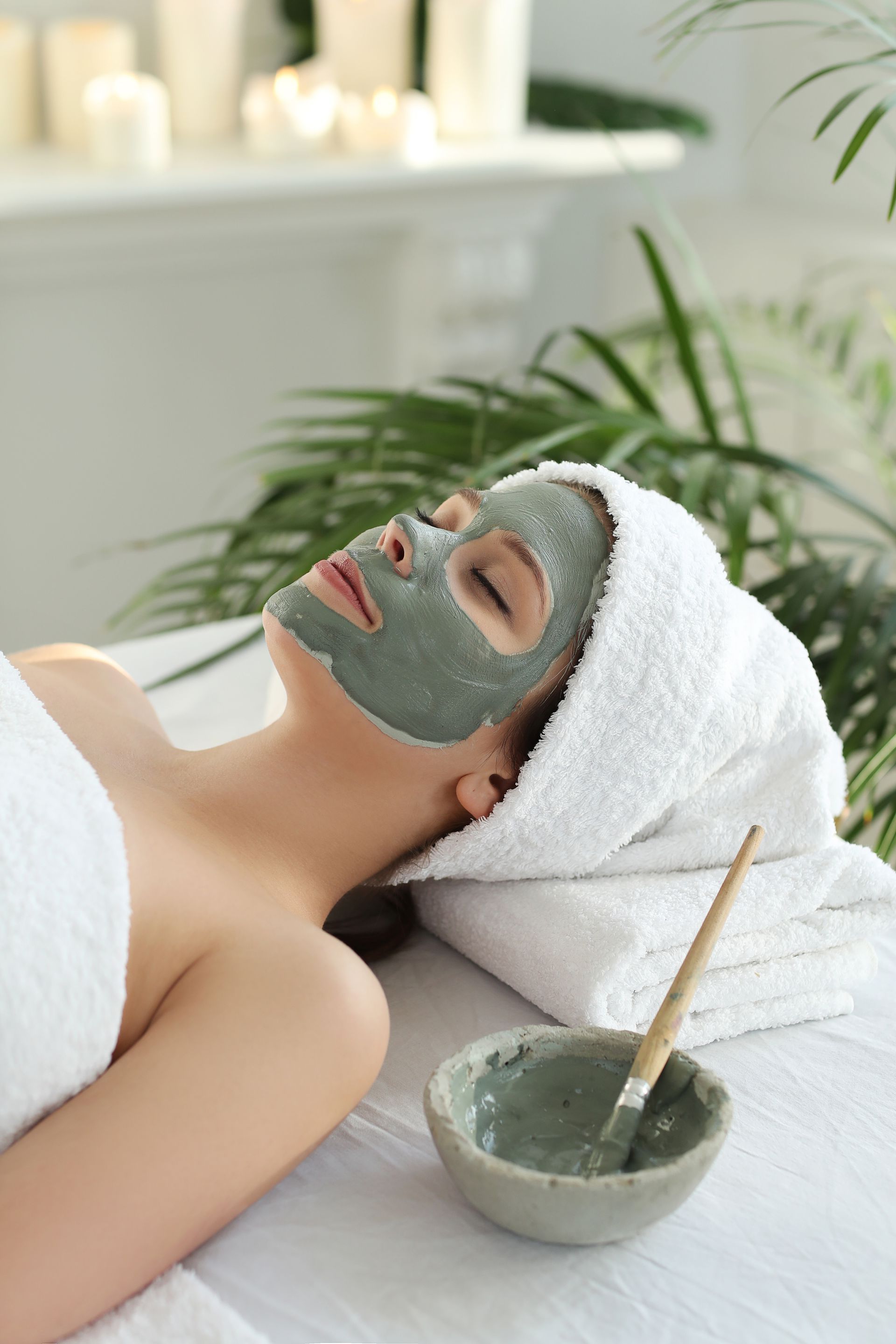 A woman is laying on a table with a clay mask on her face.