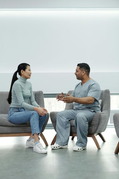 A man and a woman are sitting on a couch talking to each other.