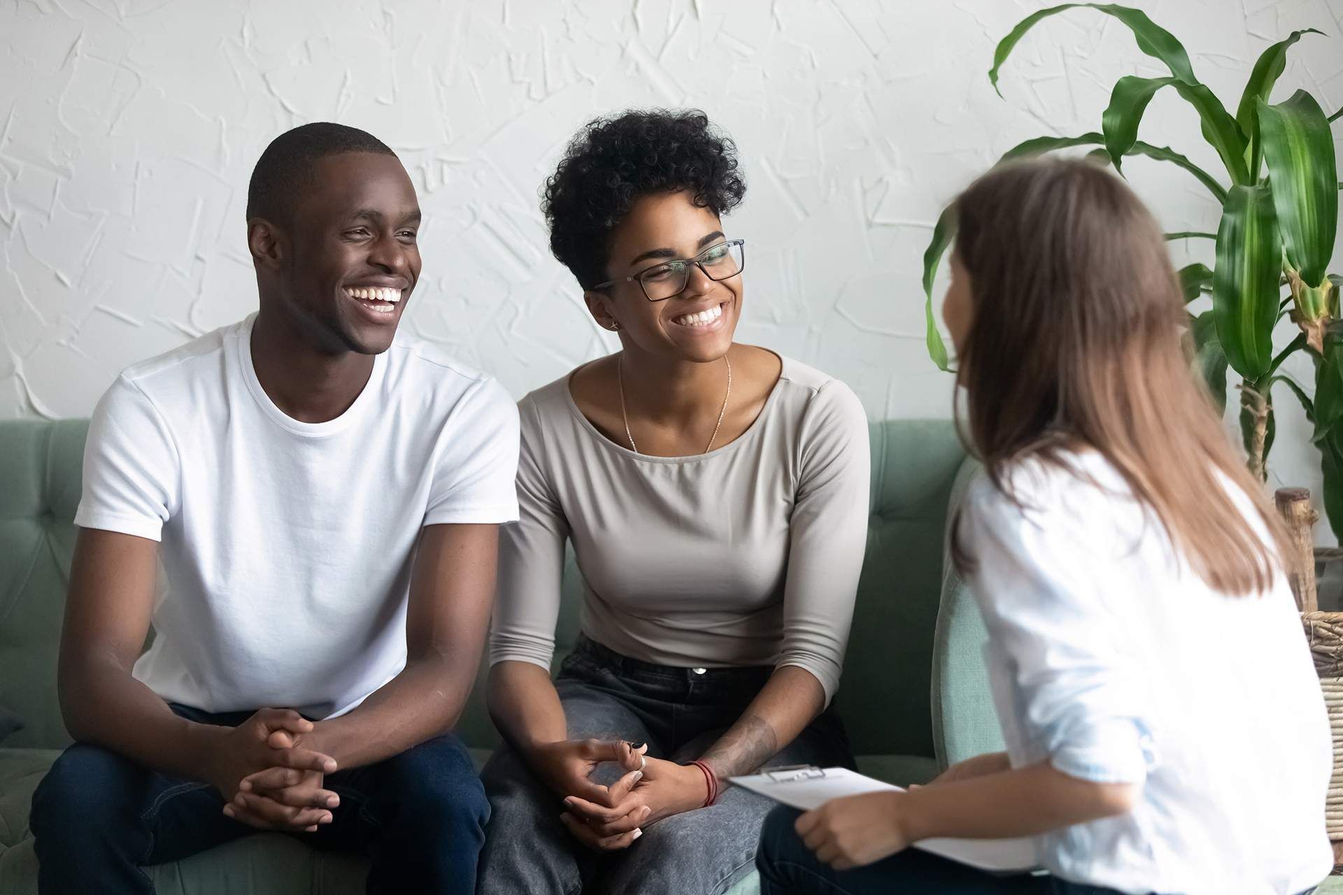 Couple smiling, talking with counselor on a sofa; a plant is in the background.