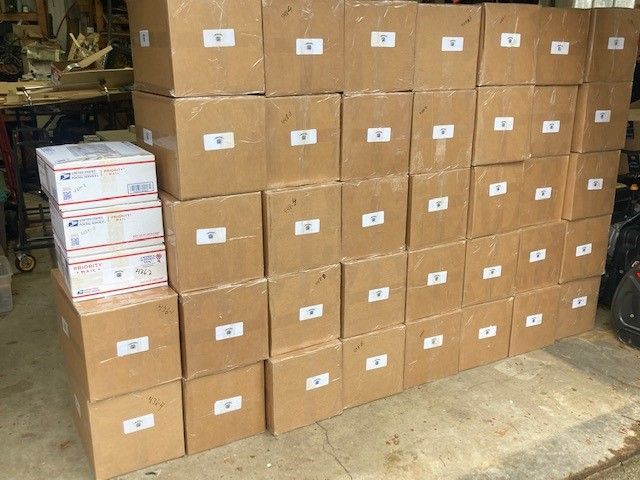 Boxes stacked on a concrete surface; mostly brown cardboard, some white USPS boxes