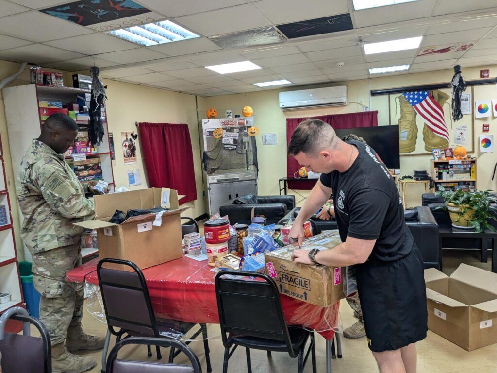 Two service members unpacking boxes in a room with snacks on a table