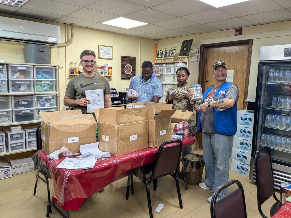 Four people stand behind a table with boxes in a room