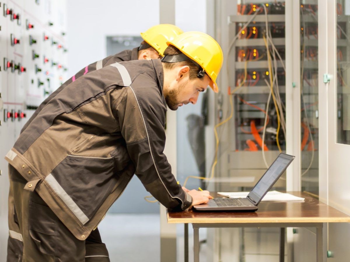 A man wearing a hard hat is working on a laptop computer.