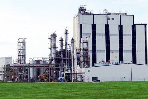 Two technicians in hard hats inspect electrical panel, one using a laptop in a control room.