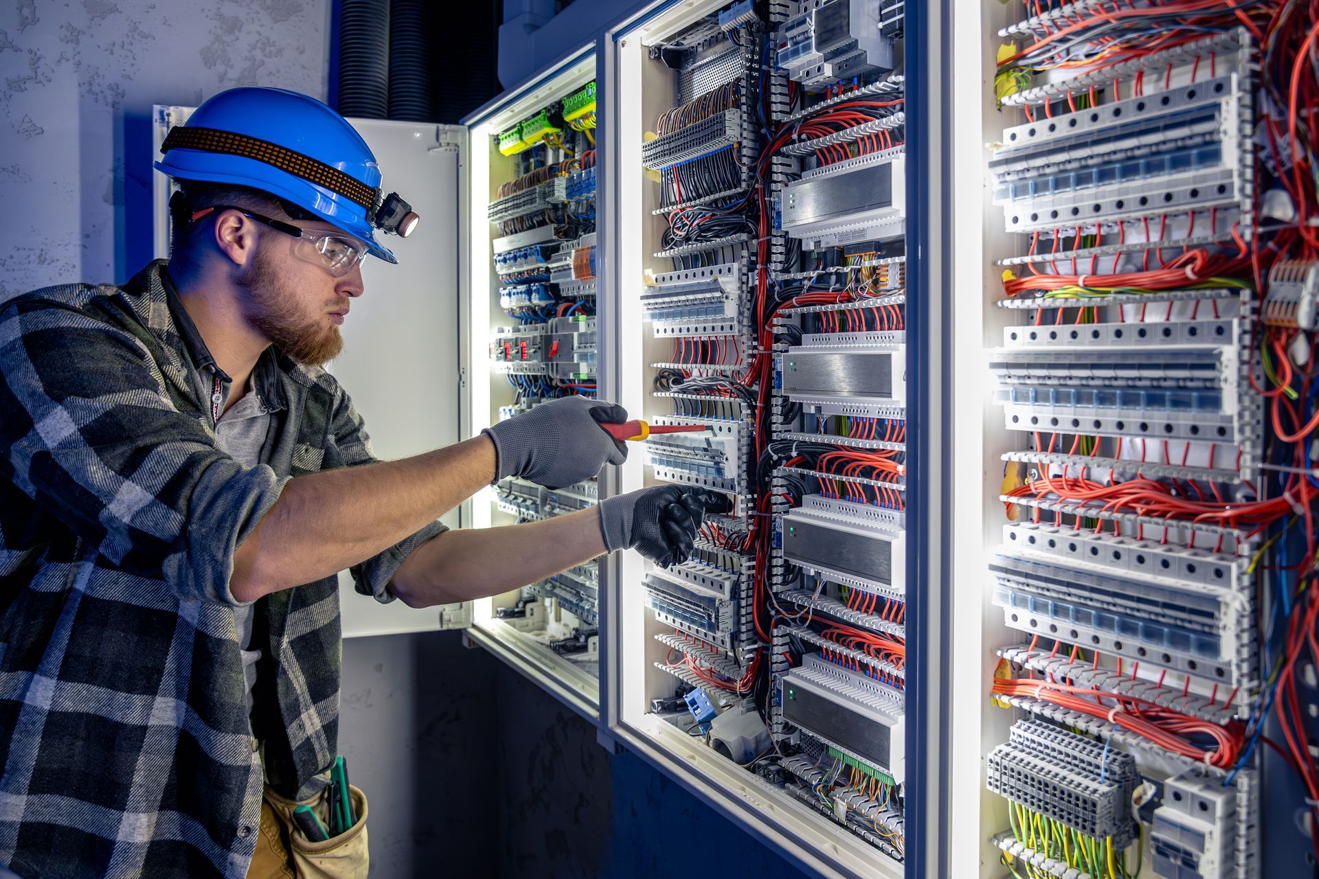 An electrician is working on a electrical panel with a screwdriver.