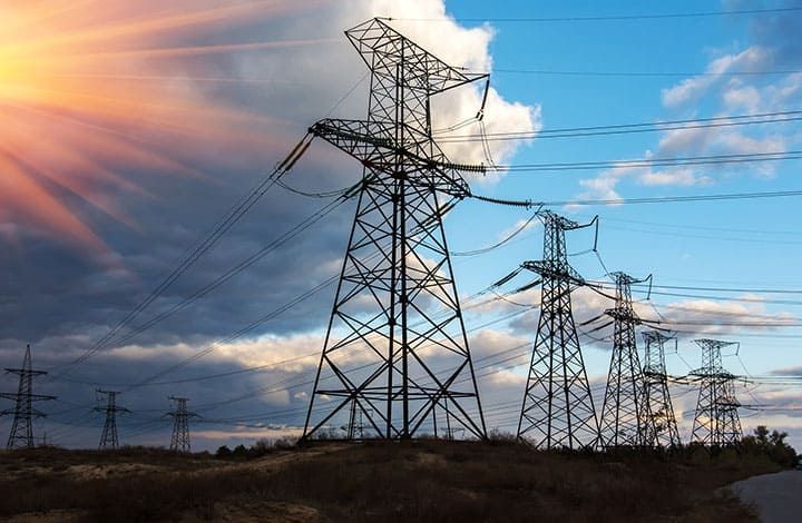 Two technicians in hard hats inspect electrical panel, one using a laptop in a control room.