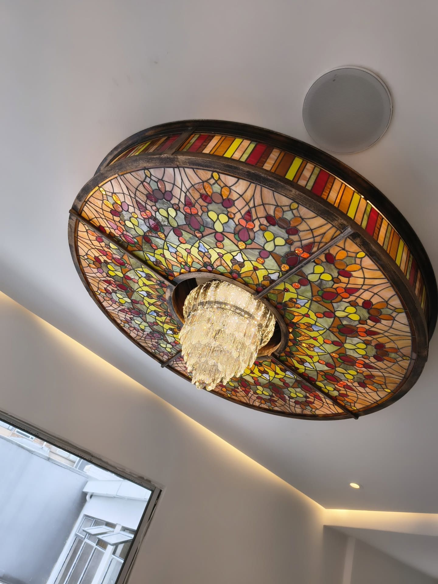 Una lámpara de techo circular de vidrieras multicolores con una araña de cristal en el centro.