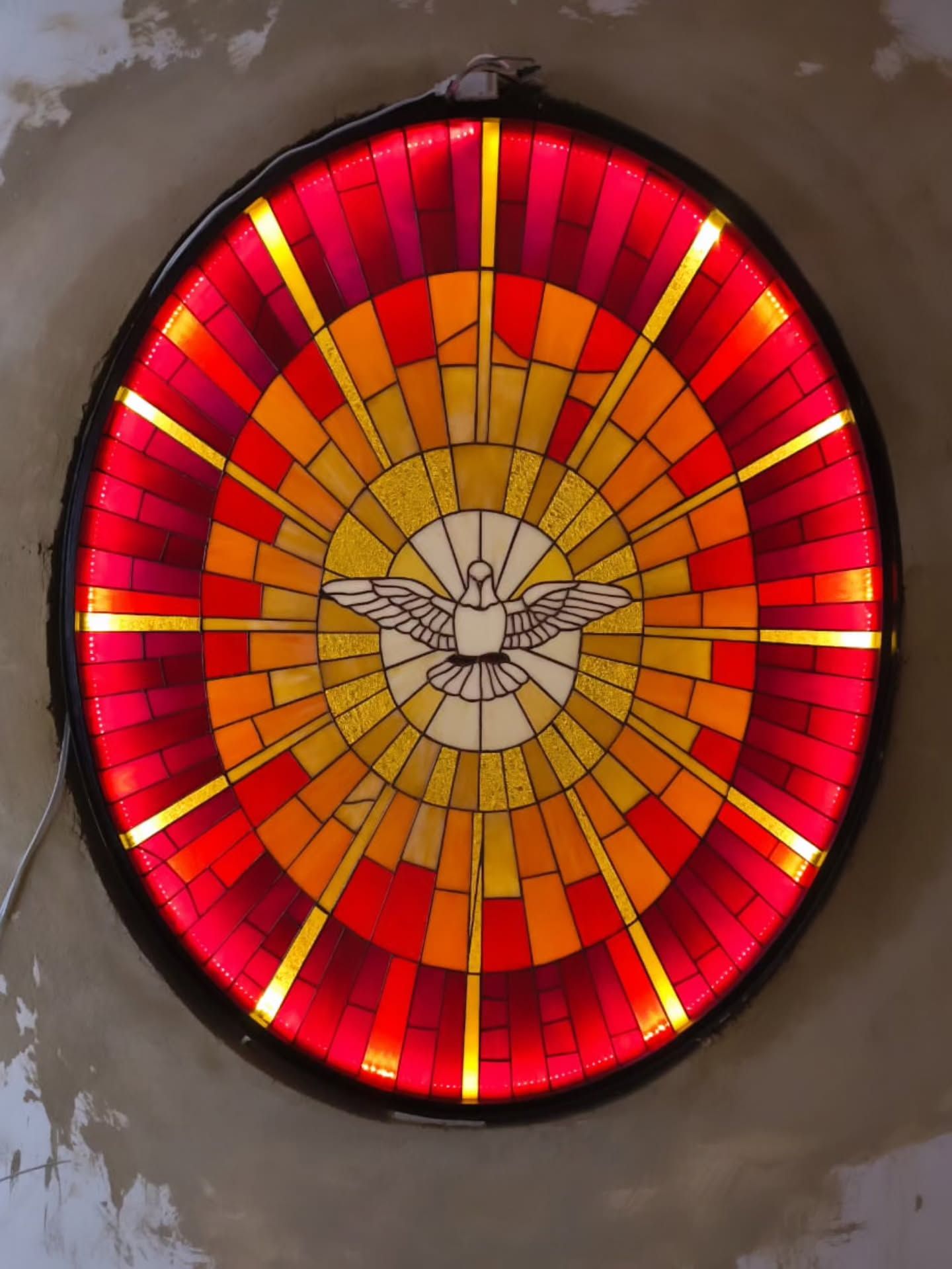 Una obra de arte circular en vidriera que presenta una paloma blanca en el centro, rodeada de bandas radiantes