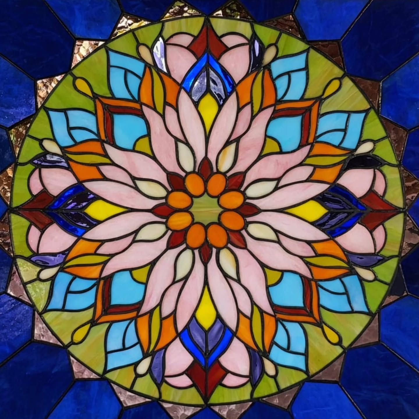 Un colorido y simétrico mandala de vidrieras con intrincados motivos florales en rosa, azul, naranja, amarillo y verde.
