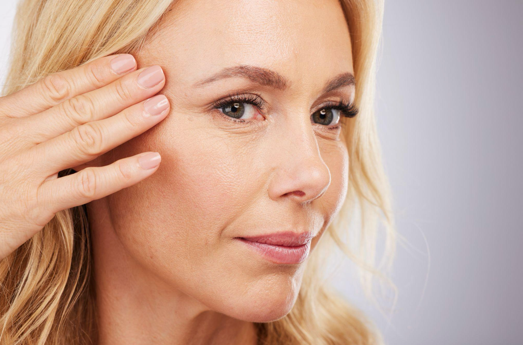 Woman smiling, seated outdoors on wooden steps, wearing denim shirt and jeans.