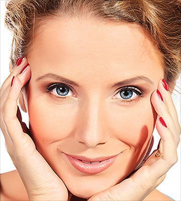 Woman with blue eyes, smiling, holding face with hands, red nail polish.