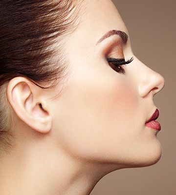 Woman's profile view, wearing eye makeup and red lipstick, against a light brown background.