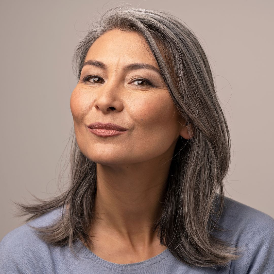 Woman with gray hair, light blue sweater, looking at the viewer with a slight smile.