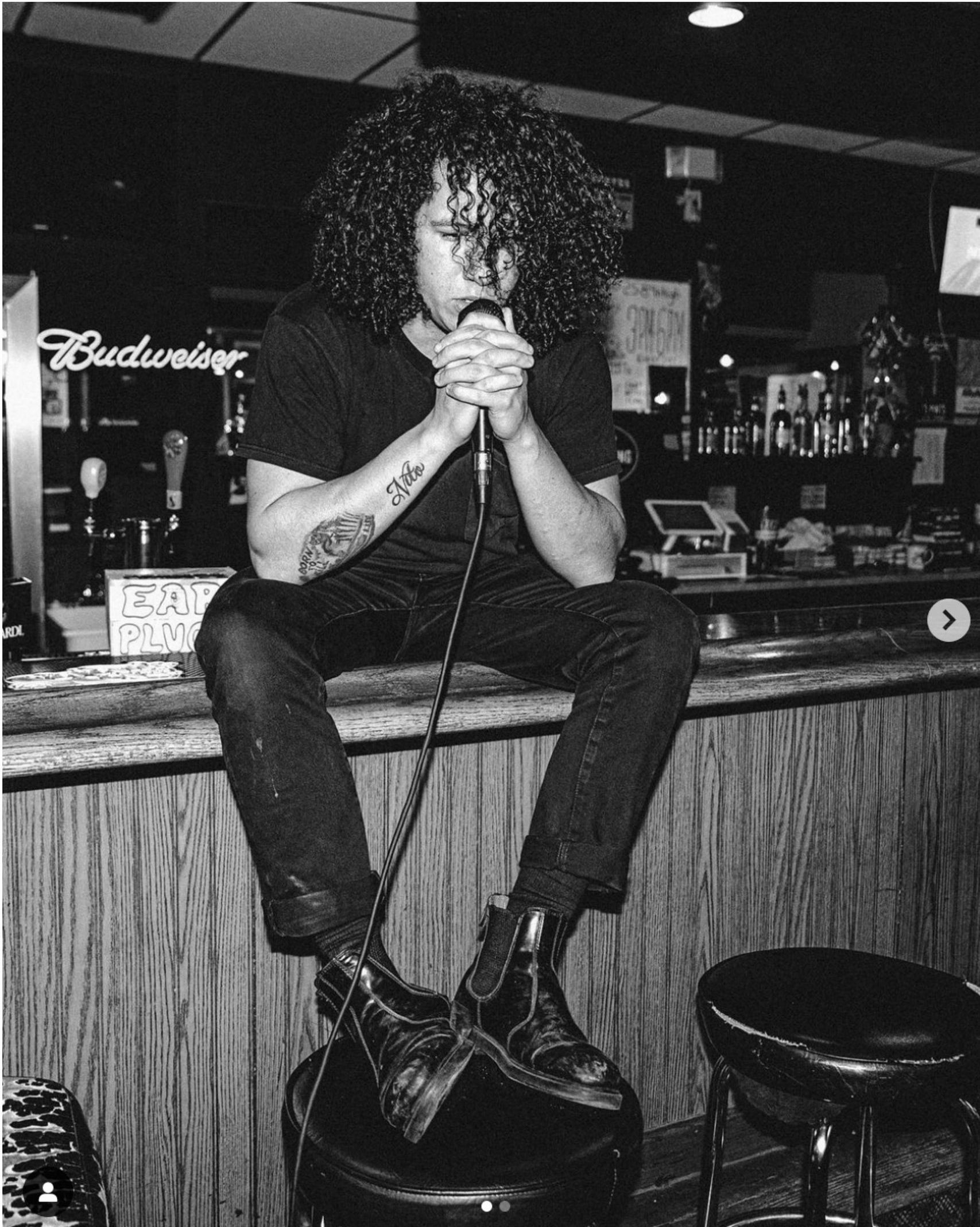 A man singing into a microphone in front of a budweiser sign