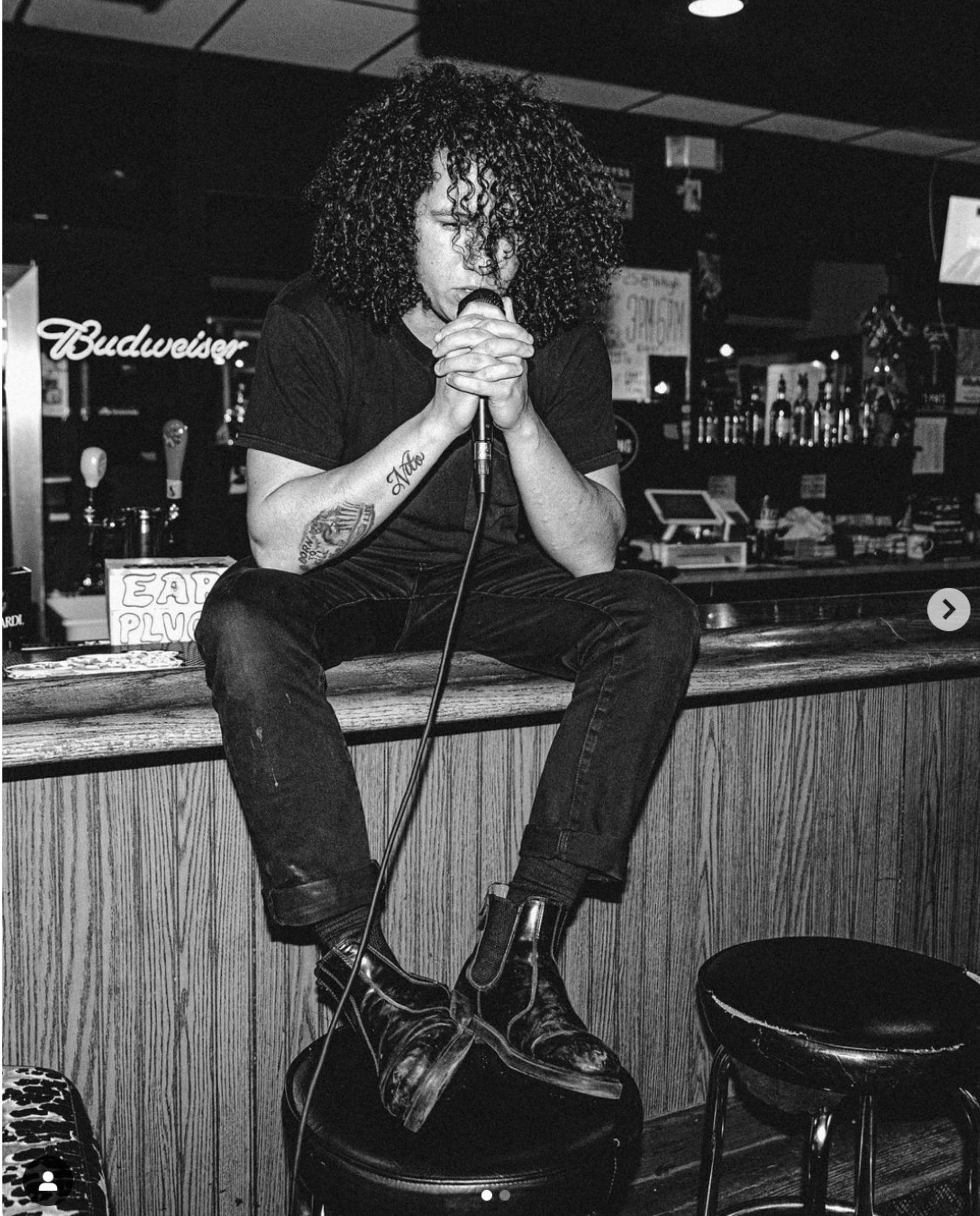 A man singing into a microphone in front of a budweiser sign