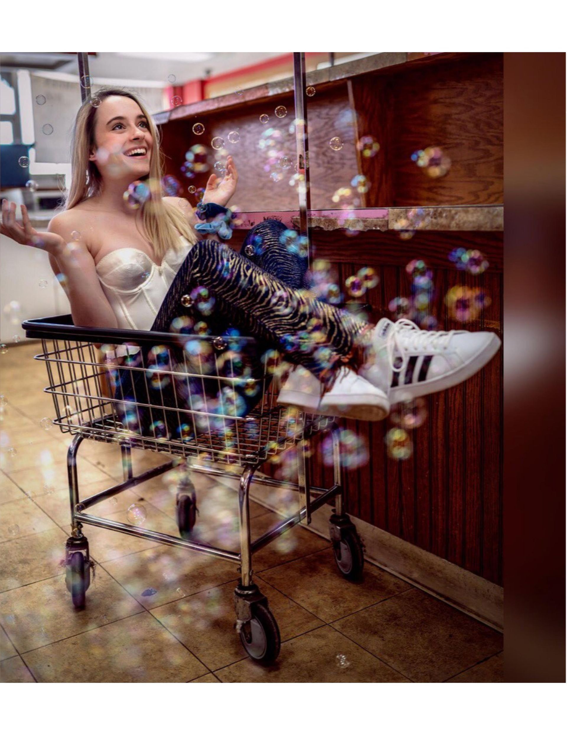A woman is sitting in a shopping cart surrounded by soap bubbles.