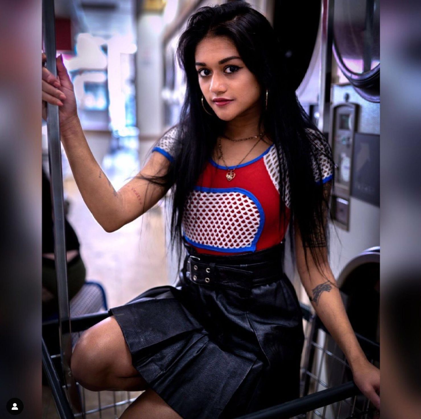 A woman in a red top and black skirt is sitting in a laundromat