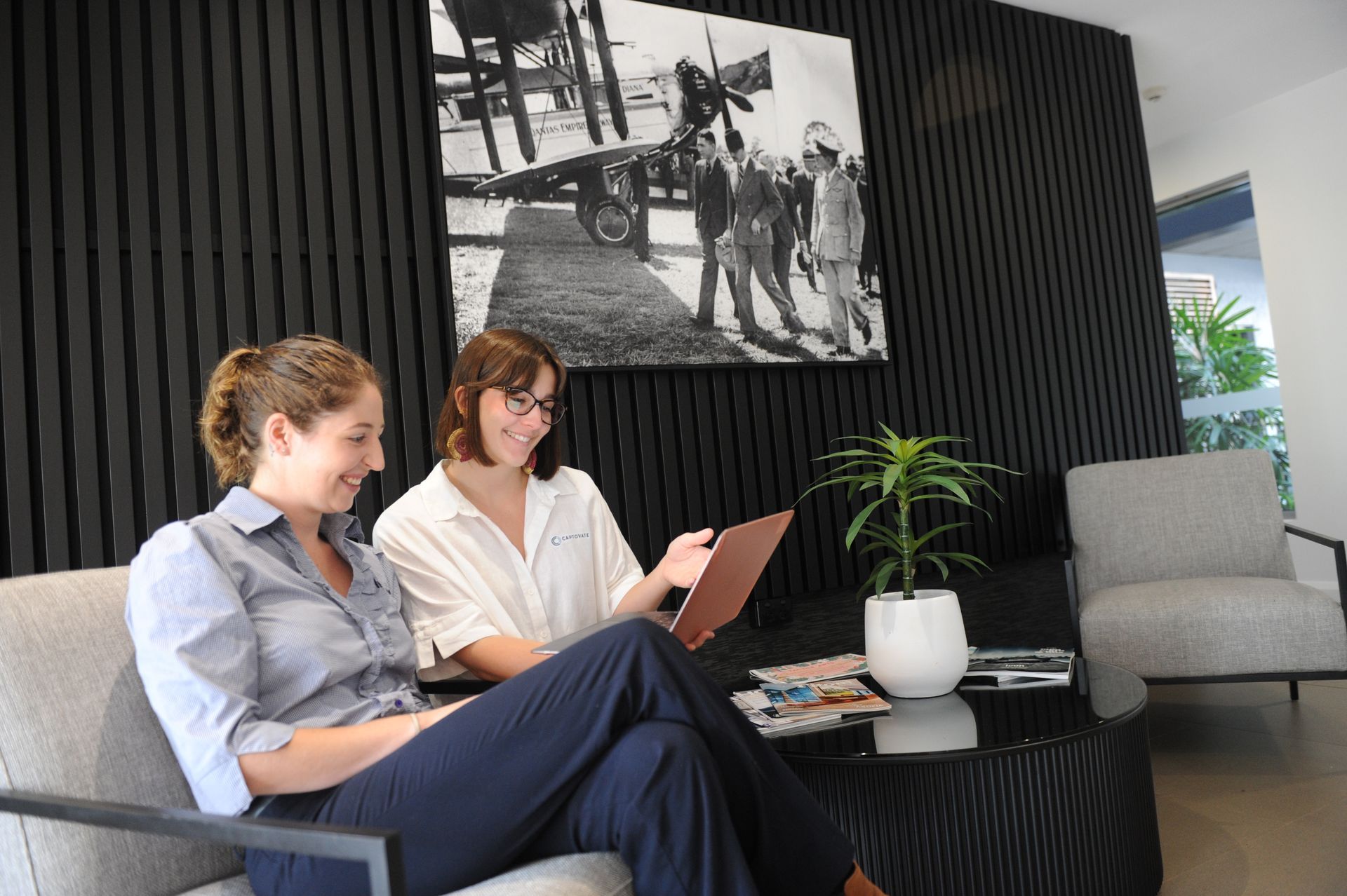 Two women are sitting on a couch looking at a laptop.