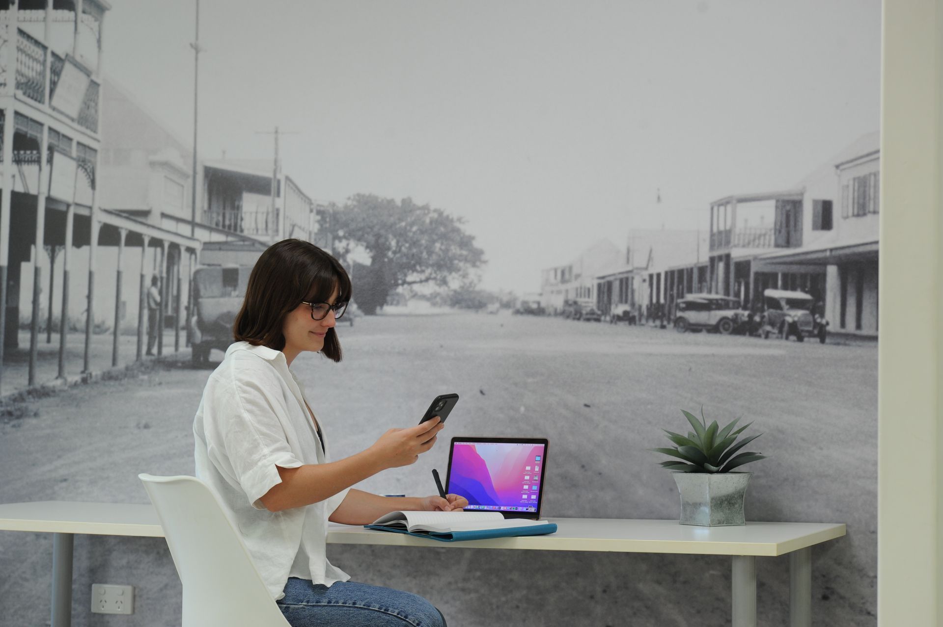 A woman is sitting at a desk with a laptop and a cell phone.