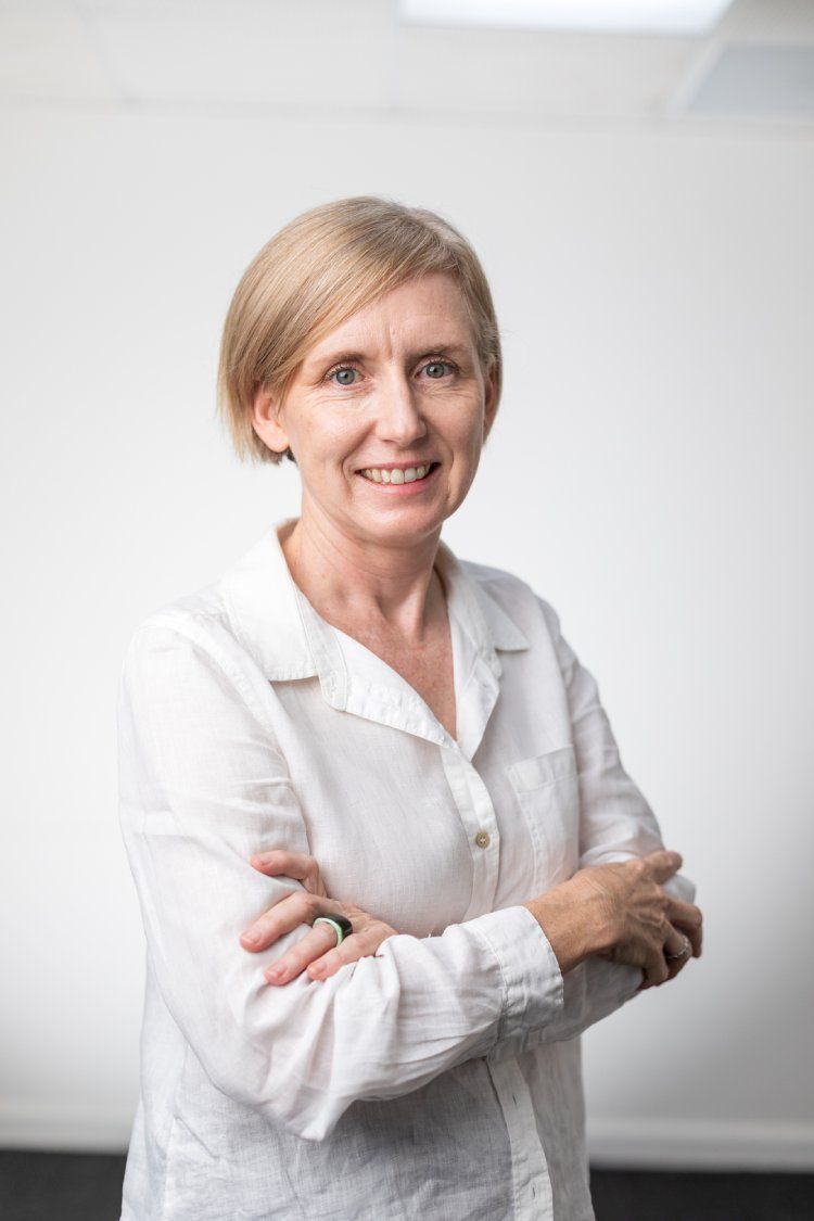 A woman in a white shirt is standing with her arms crossed and smiling.