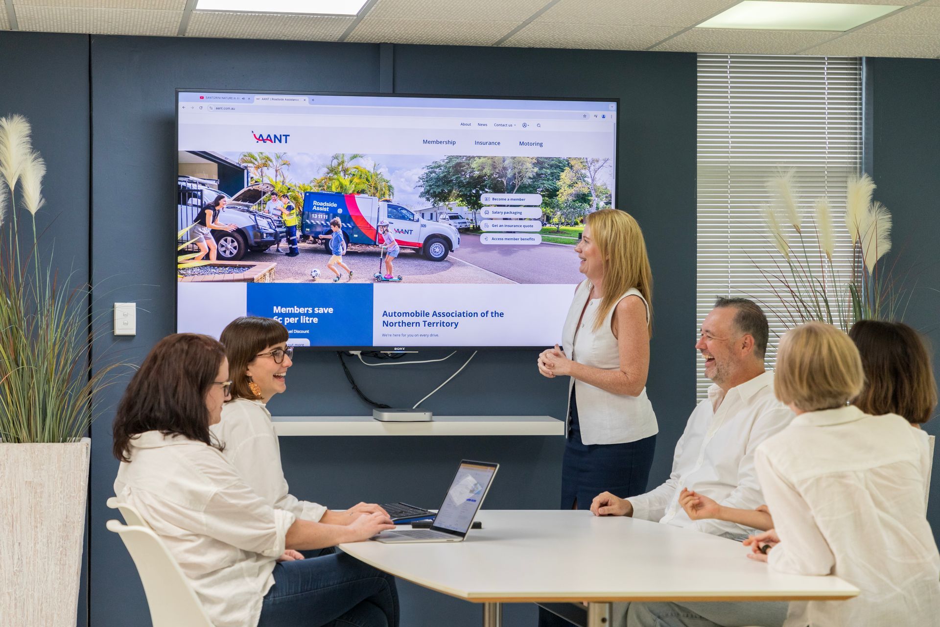 A group of people are sitting around a table in front of a large screen.