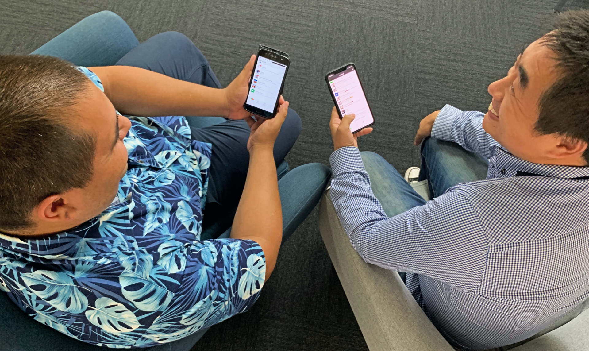 Two men are sitting on the floor looking at their phones.