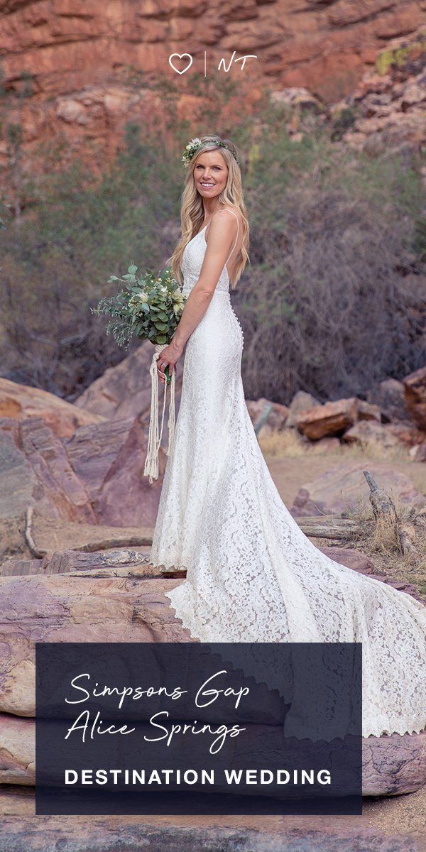 A woman in a wedding dress is standing on a rock holding a bouquet of flowers.