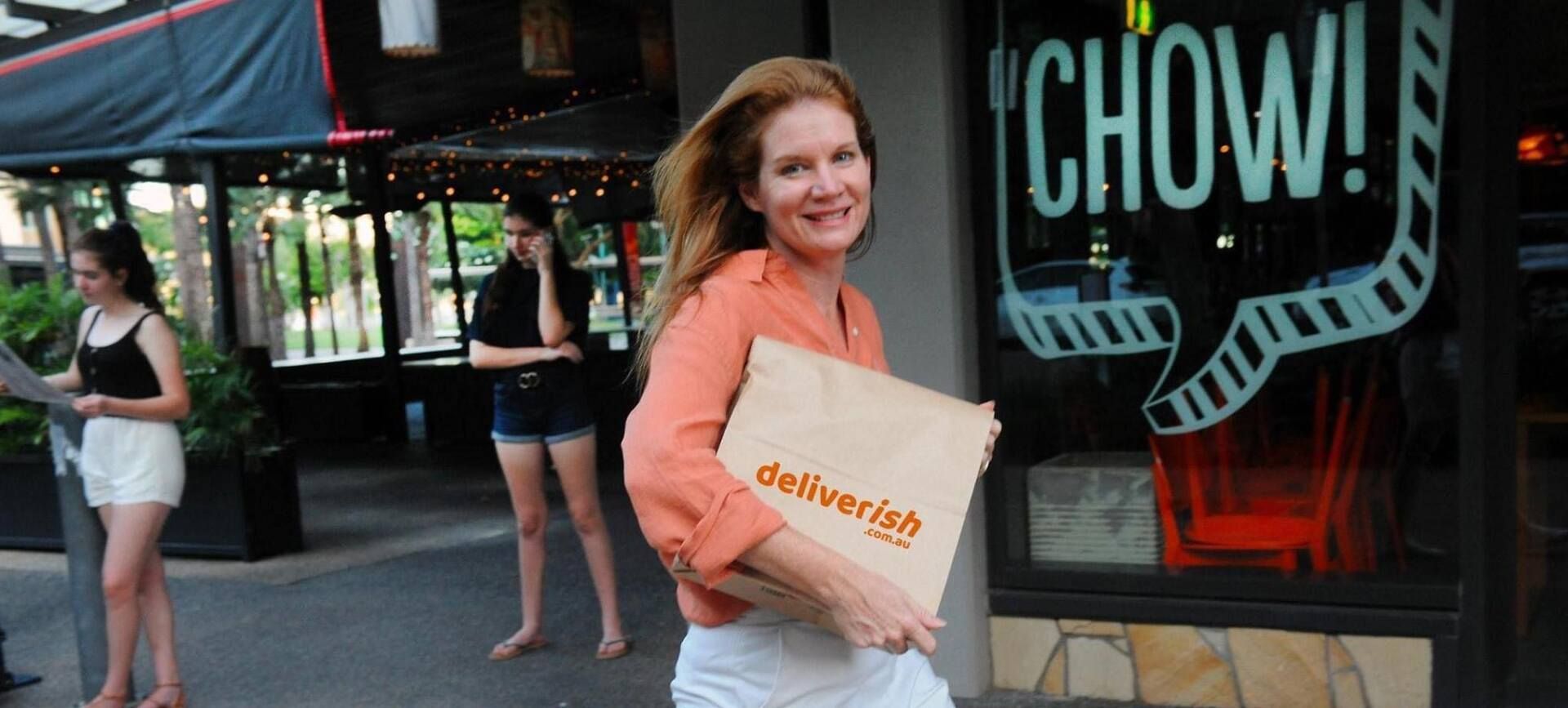 A woman is carrying a bag in front of a restaurant.