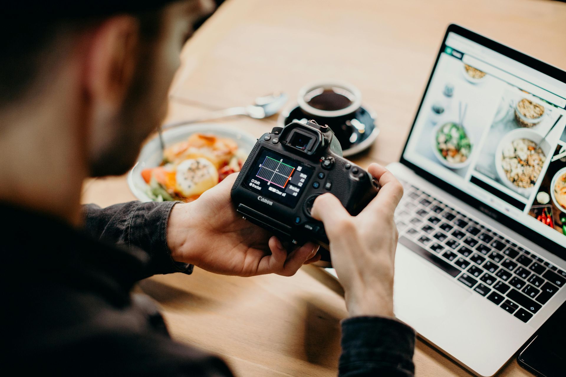 A man is holding a camera in front of a laptop computer.