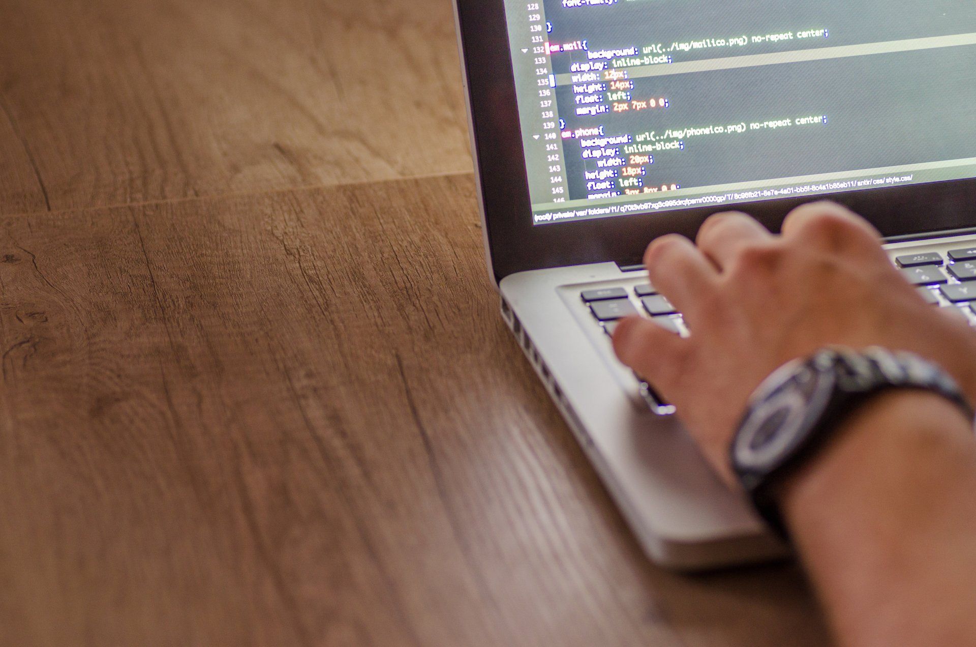 A person wearing a watch is typing on a laptop