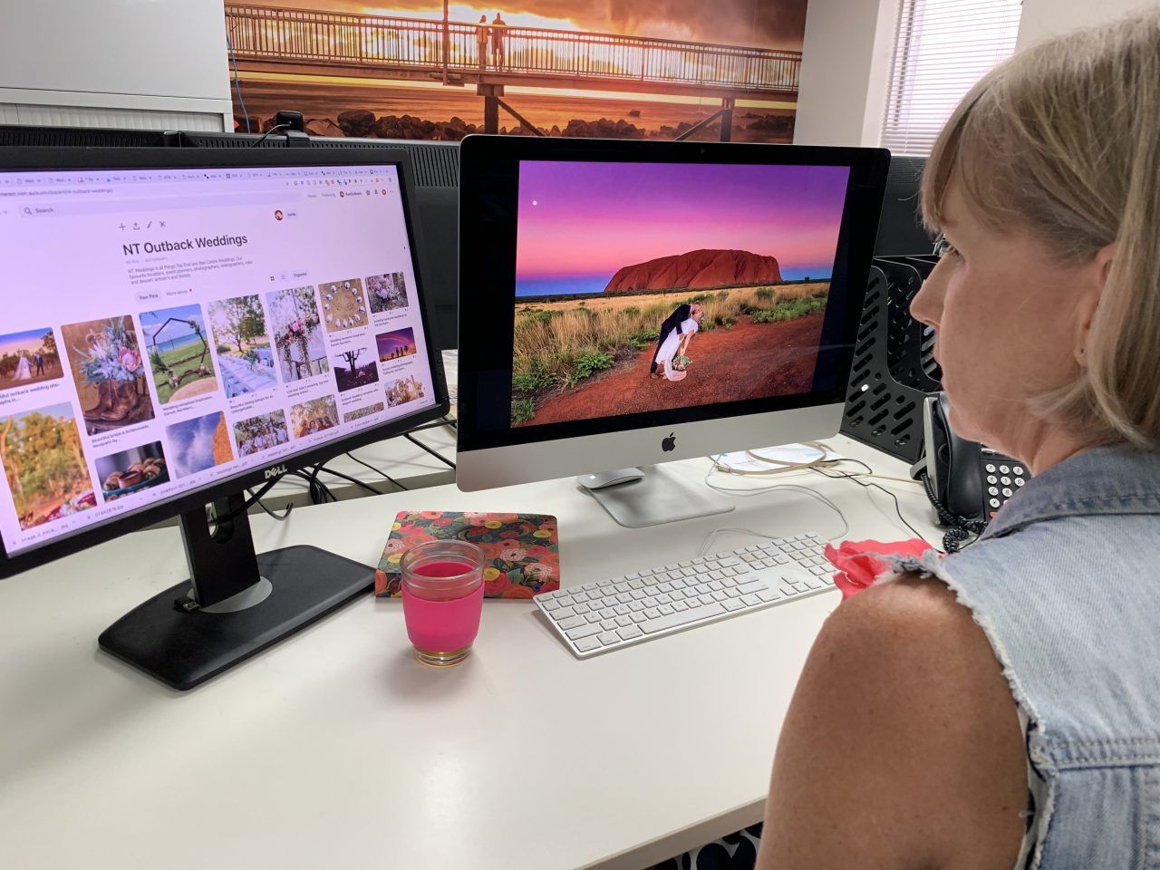 A woman is sitting at a desk looking at two computer monitors.