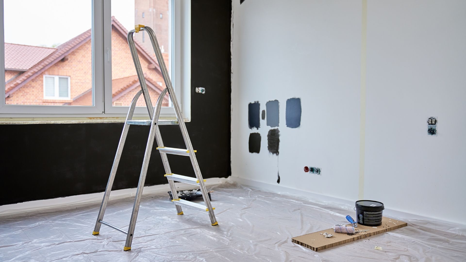Ladder in a room with black and white painted walls, paint samples, and a paint bucket.