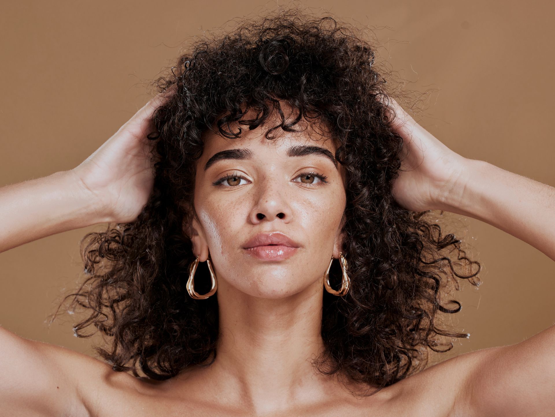 a woman with curly hair and hoop earrings is holding her hair .
