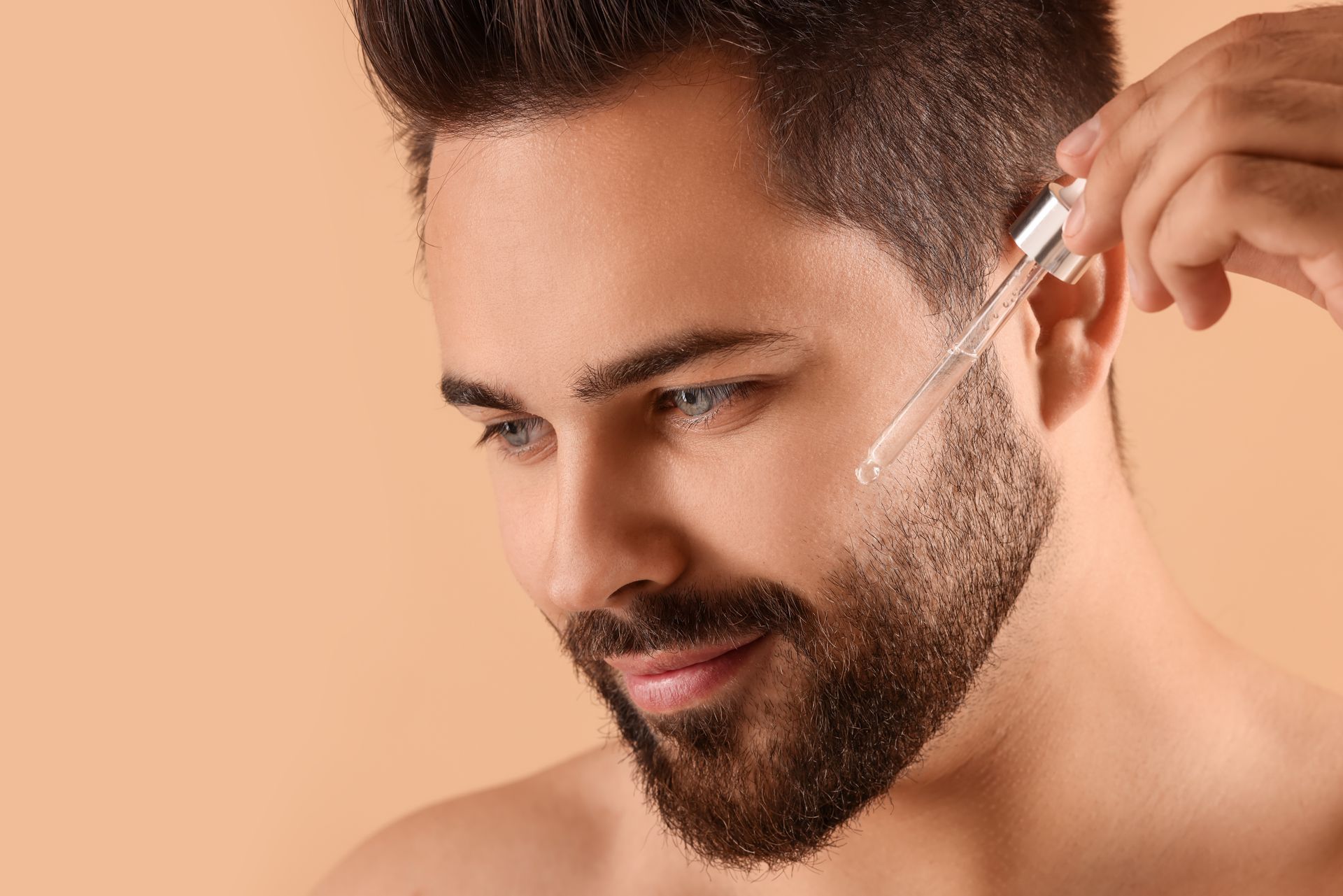 a man with a beard is applying a serum to his face .
