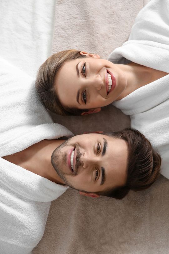 a man and a woman in bathrobes are laying next to each other on a bed .