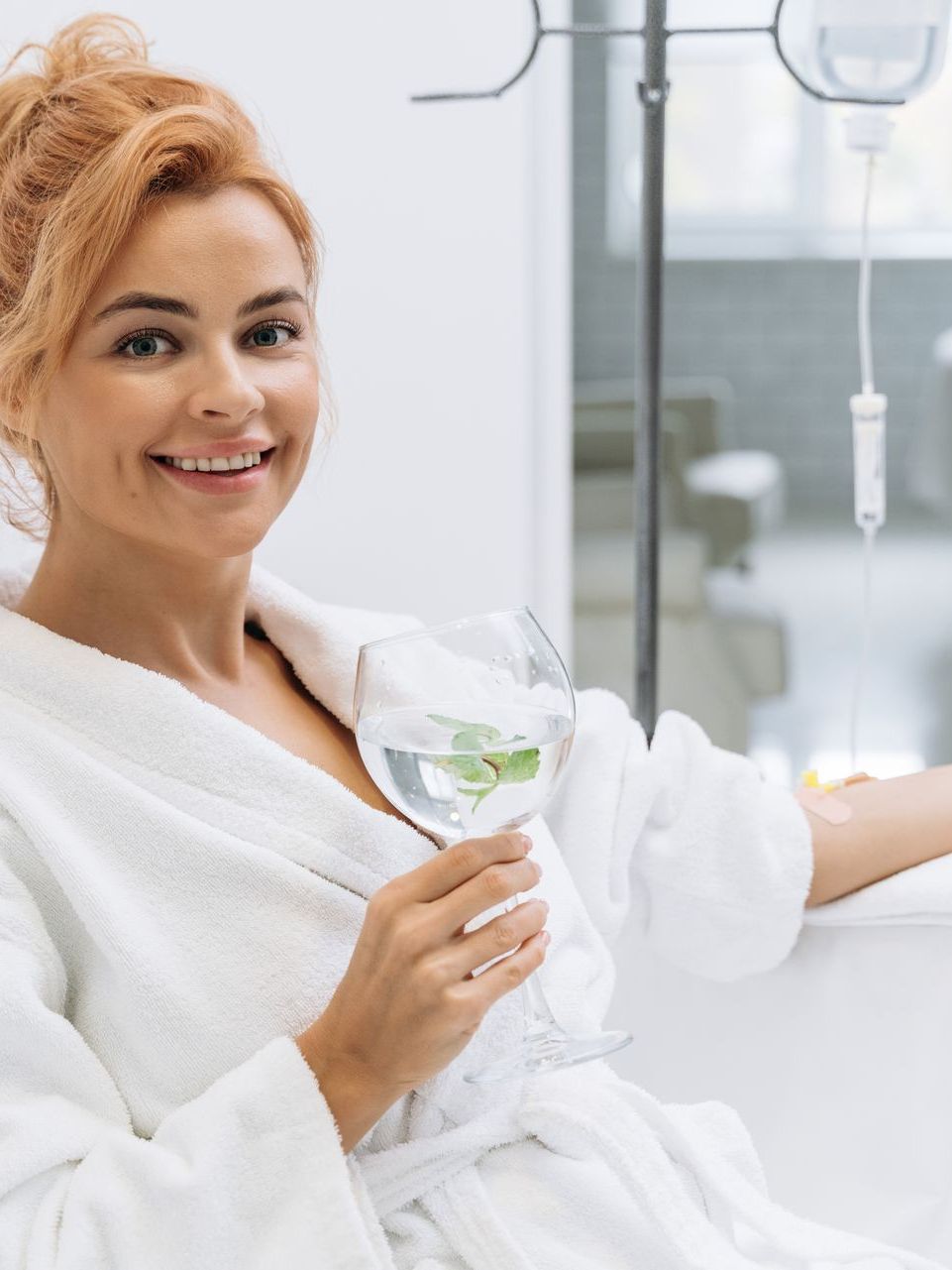 a woman in a bathrobe is holding a glass of water .