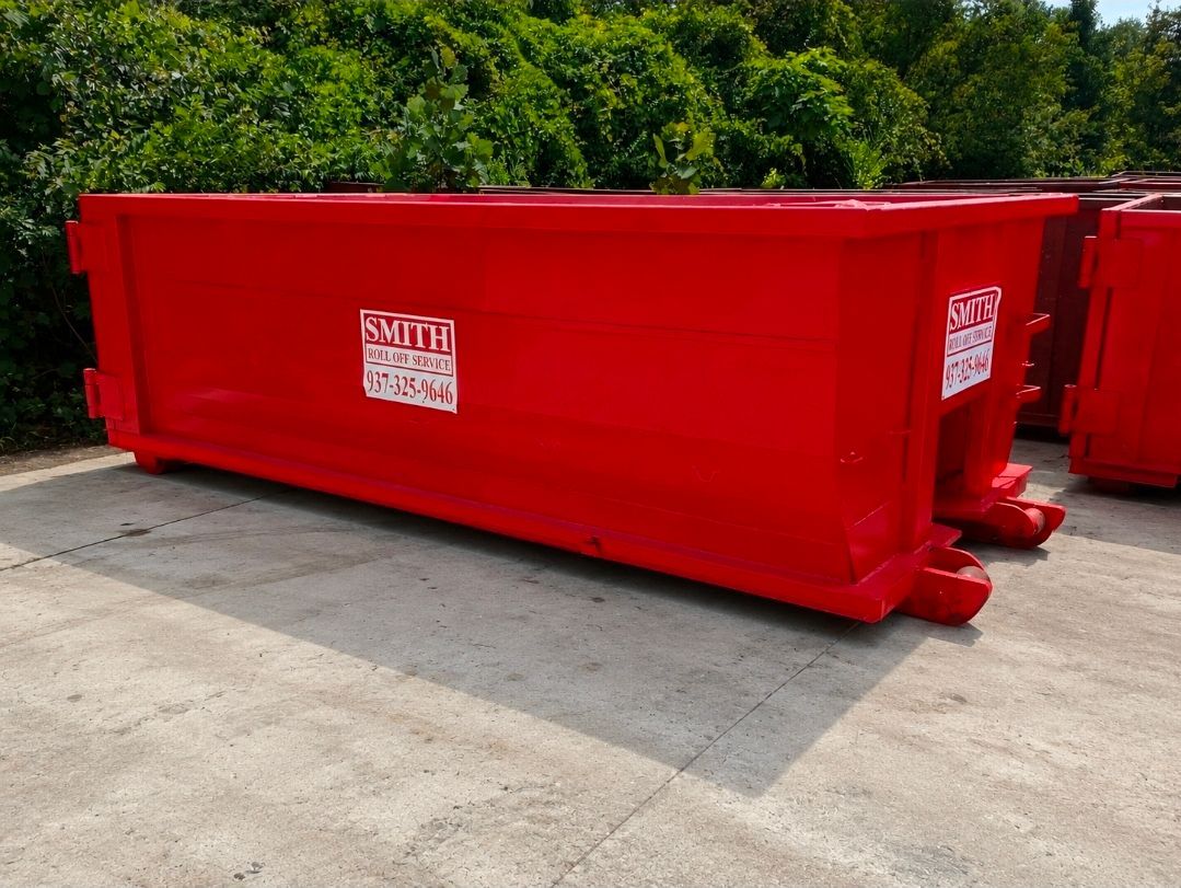 A large green dumpster is parked on a brick driveway in front of a building. A large green dumpster is parked on a brick driveway in front of a building.