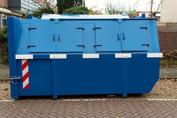 A blue dumpster is parked on the side of the road