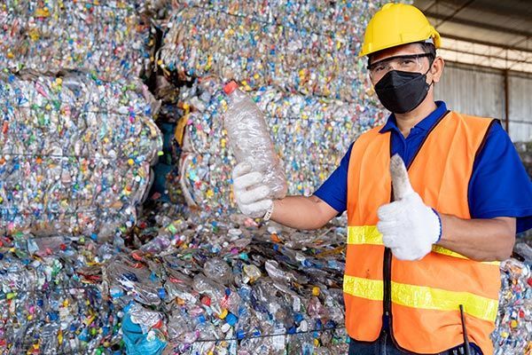 A man wearing a hard hat and safety vest is holding a plastic bottle and giving a thumbs up.