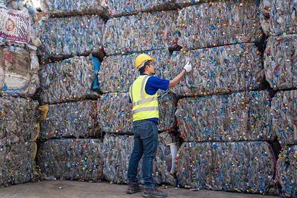 A man is standing in front of a pile of plastic bottles.