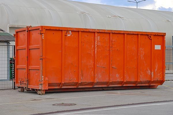 A large orange dumpster is parked in front of a building.