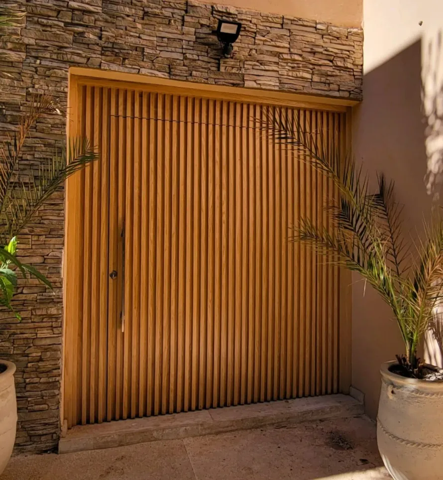 Porte à claire-voie en bois encastrée dans un mur de pierre, avec des plantes en pot de chaque côté.