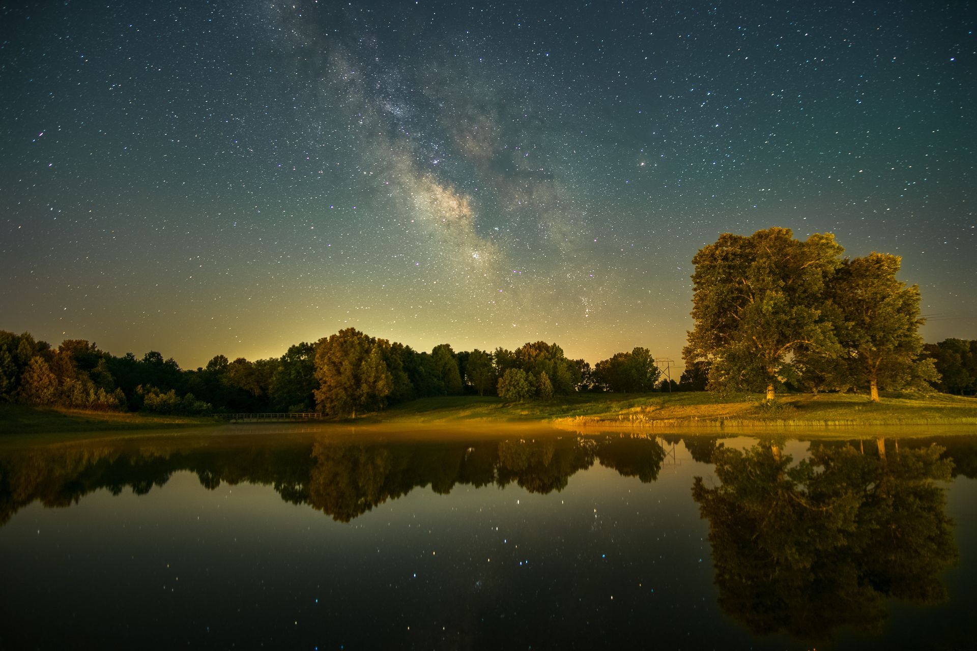 The sun is setting over a river with a tree in the foreground.