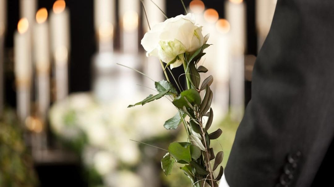 A man in a suit is holding a white rose at a funeral.